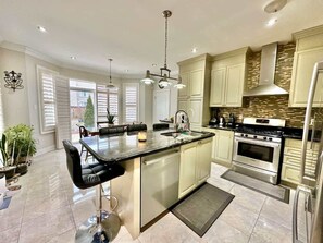 A modern kitchen with a central island, stainless steel appliances, and a dining area with black chairs. - Spacious 4BR Home with Private Yard & Fast WiFi (Brampton)