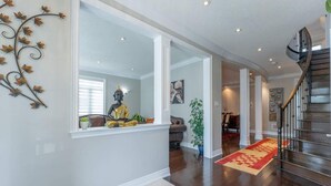 A spacious hallway with a wooden staircase, a Buddha statue, and a decorative metal vine on the wall. - Spacious 4BR Home with Private Yard & Fast WiFi (Brampton)