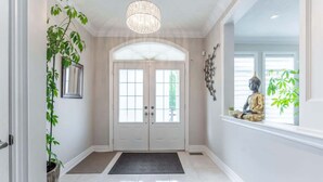 A hallway with a double door, a potted plant, a hanging light fixture, and a statue on the windowsill. - Spacious 4BR Home with Private Yard & Fast WiFi (Brampton)