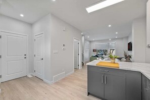 A modern kitchen with grey cabinets, a white countertop, and a wooden cutting board.