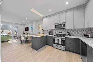 A modern kitchen with grey cabinets, a central island, a built-in oven, and a microwave.
