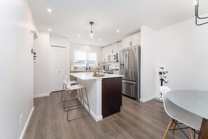 Una cocina moderna con armarios blancos, electrodomésticos de acero inoxidable y una isla central con taburetes de bar.