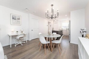 Una cocina moderna con armarios blancos, un comedor con una mesa redonda y sillas, y una araña.