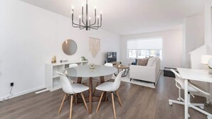 Uma sala de estar moderna com uma mesa de jantar redonda, cadeiras brancas, um sofá branco e uma escrivaninha branca.
