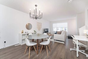 Una sala de estar moderna con una mesa redonda de comedor, sillas blancas, un sofá blanco y un escritorio blanco.