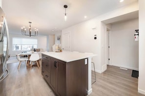 A modern kitchen with a central island, wooden cabinets, and a dining area with a white table and chairs.