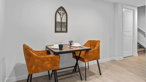 Een eetgedeelte met een tafel gedekt voor twee personen, twee oranje stoelen, een decoratieve spiegel en een trap op de achtergrond.