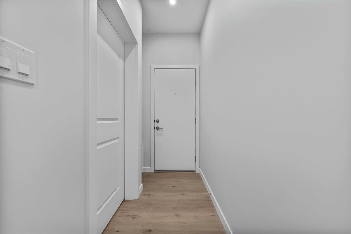 A narrow hallway with white walls and wooden flooring, leading to a closed door.