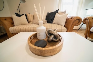 A living room with a brown leather sofa, a white table, and a wooden tray with a snake and a candle. - Foundry Farm Cottage (Hexham)
