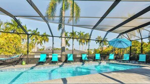A swimming pool with a covered area, surrounded by palm trees and a building in the background.
