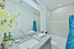 Un bagno moderno con un lavabo in granito, uno specchio grande, una doccia con tenda blu e una pianta di orchidea in vaso.
