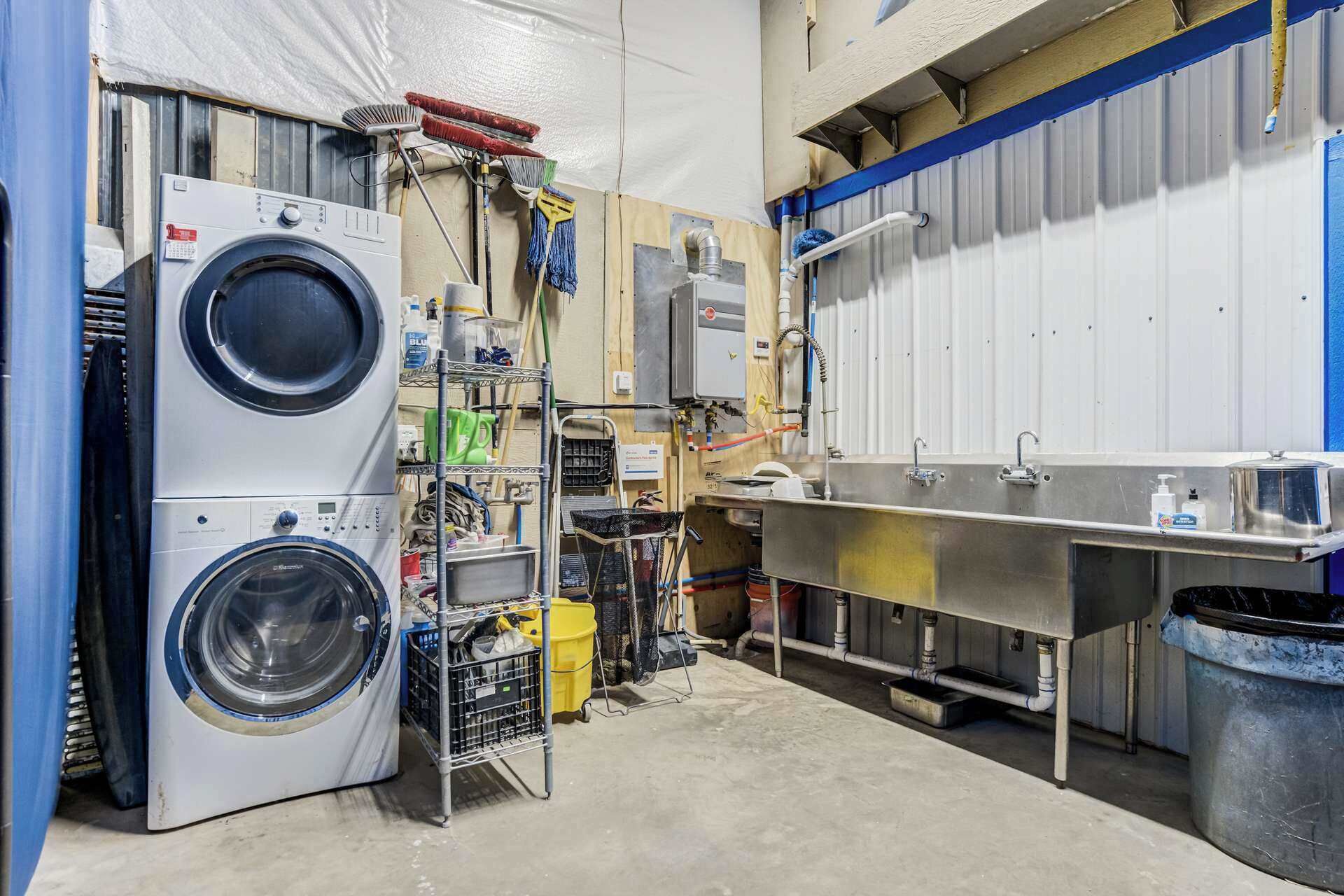 Een wasserette met twee gestapelde wasmachines, een metalen gootsteen en verschillende schoonmaakmiddelen.