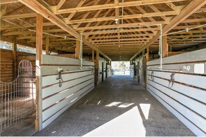 A covered barn with metal gates and a metal pen on the left, and a row of stalls on the right.