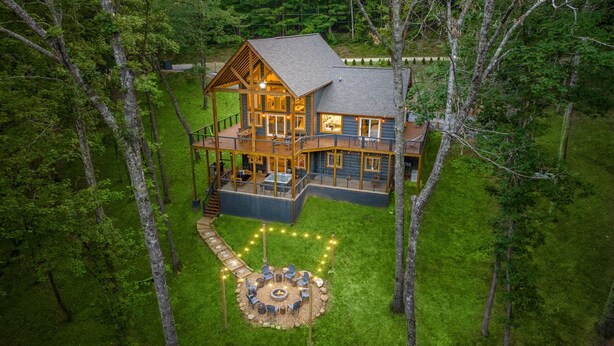 A large wooden cabin with multiple decks, a fire pit, and a surrounding grassy area. - Spacious 5-bedroom house/ Game Room/Pool Table/Firepit/HotTub/Generator (Blue Ridge)