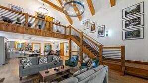 A spacious living area with a staircase, wooden beams, and a kitchen in the background. - Spacious 5-bedroom house/ Game Room/Pool Table/Firepit/HotTub/Generator (Blue Ridge)