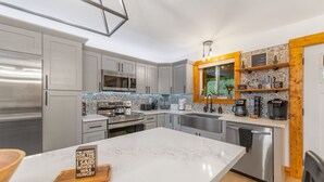 A modern kitchen with grey cabinets, stainless steel appliances, a marble countertop, and a wooden-framed window. - Spacious 5-bedroom house/ Game Room/Pool Table/Firepit/HotTub/Generator (Blue Ridge)