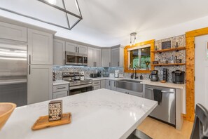 A modern kitchen with grey cabinets, stainless steel appliances, a marble countertop, and a wooden-framed window. - Spacious 5-bedroom house/ Game Room/Pool Table/Firepit/HotTub/Generator (Blue Ridge)