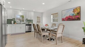 A modern kitchen with white cabinets, a stainless steel refrigerator, and a dining area with a glass table and four chairs. - Cozy Home in Newton (Newton)