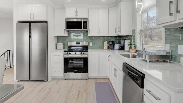 A modern kitchen with white cabinets, stainless steel appliances, and a green tiled backsplash. - Cozy Home in Newton (Newton)