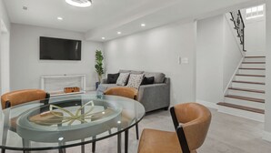 A modern living room with a glass table, leather chairs, a grey sofa, and a staircase. - Cozy Home in Newton (Newton)