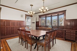 A dining room with a wooden table and chairs, a chandelier, stained glass windows, and wooden paneling. - The Lyon House at Loring Park (Minneapolis)