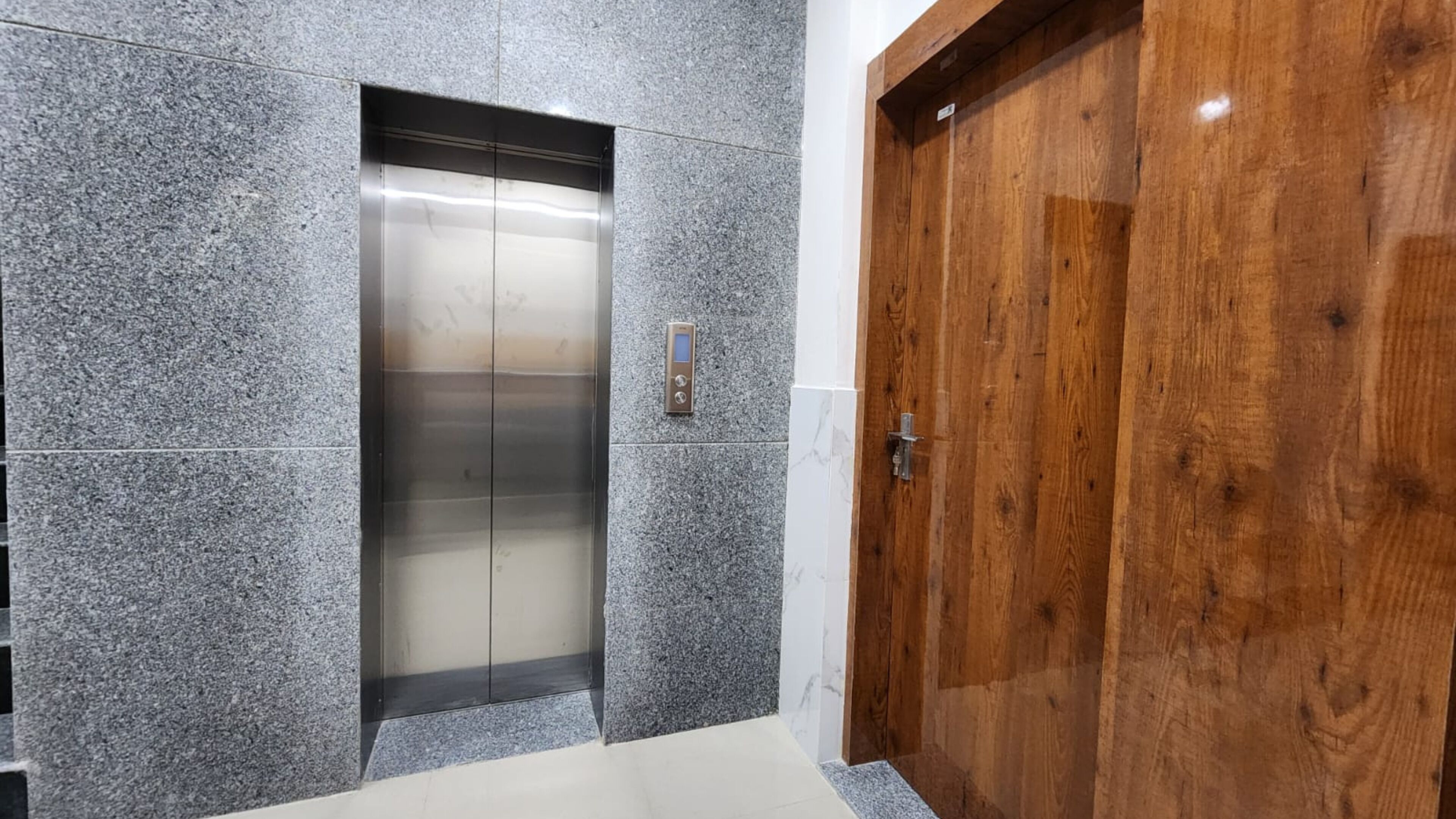 An elevator with a digital control panel, a wooden door, and granite walls.