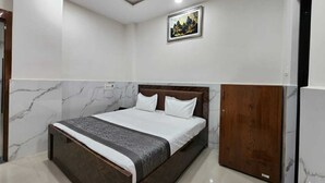 A bedroom with a bed, a wooden wardrobe, and a painting on the wall. - Hotel The Orchid Plaza (Samba)