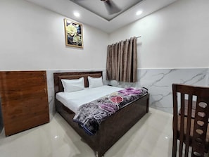 Un dormitorio con cama, armario de madera, una silla, cortina e imagen enmarcada en la pared.