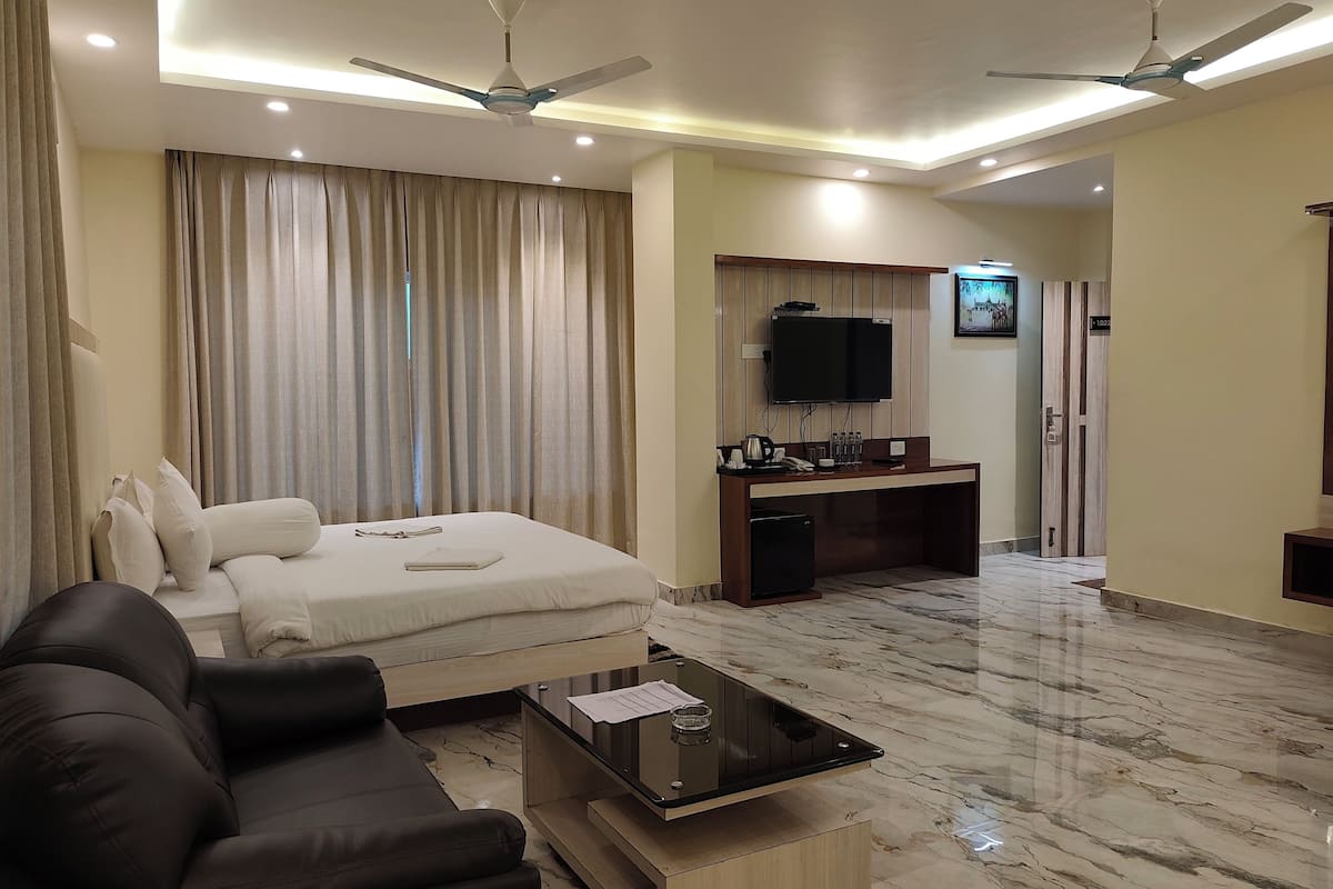 A hotel room with a bed, a sofa, a desk with a computer, a TV, and a ceiling fan.