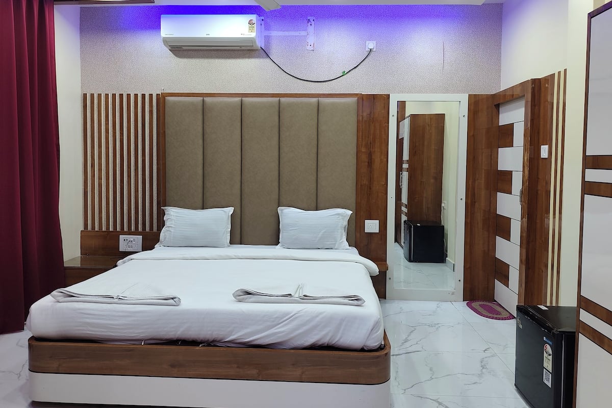 A hotel room with a bed, a ceiling fan, an air conditioning unit, and a small refrigerator.