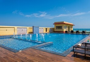 Una piscina con chorros de agua, un edificio pequeño y vista al océano.