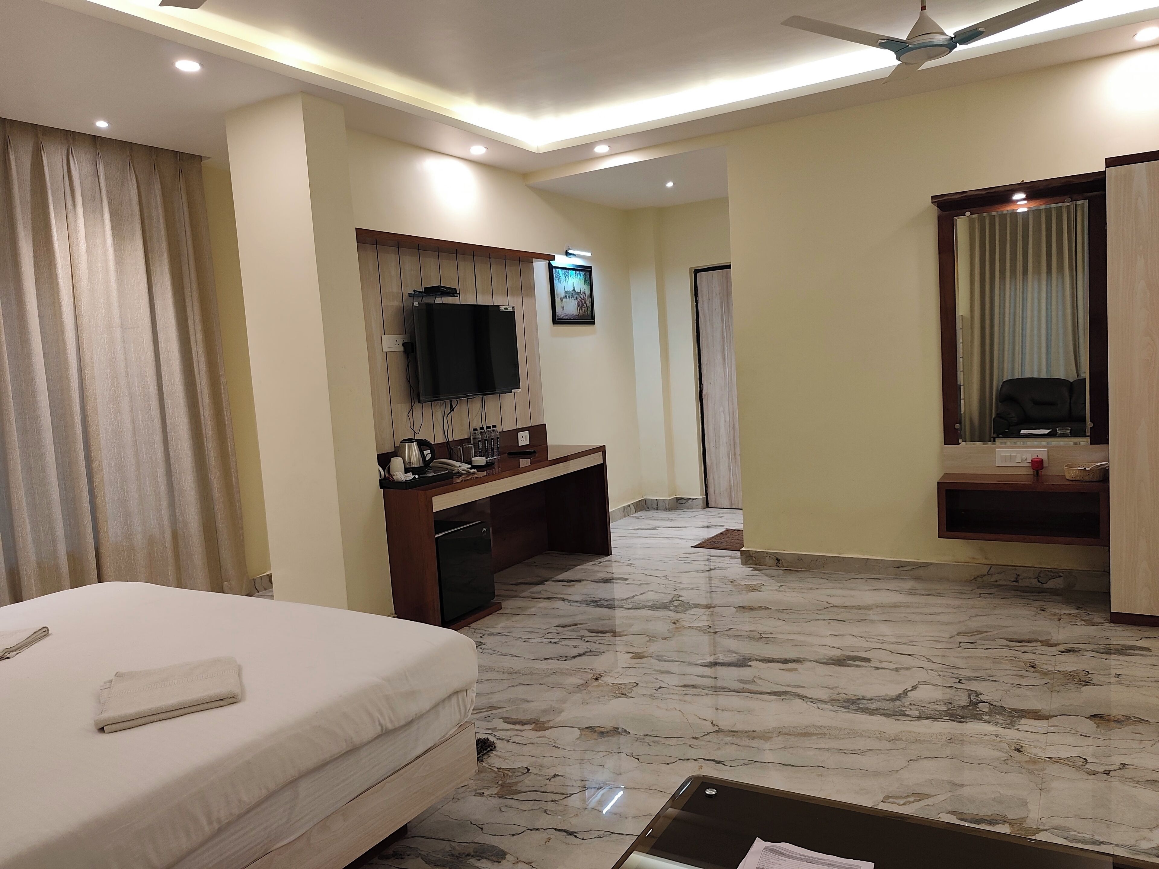 A hotel room with a bed, a desk with a flat-screen TV, a mirror, and a ceiling fan.