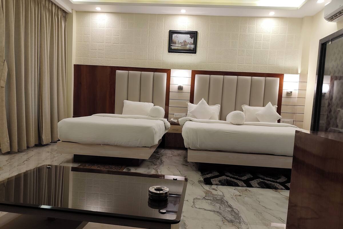 A hotel room with two beds, a marble floor, a glass coffee table, and a framed picture on the wall.