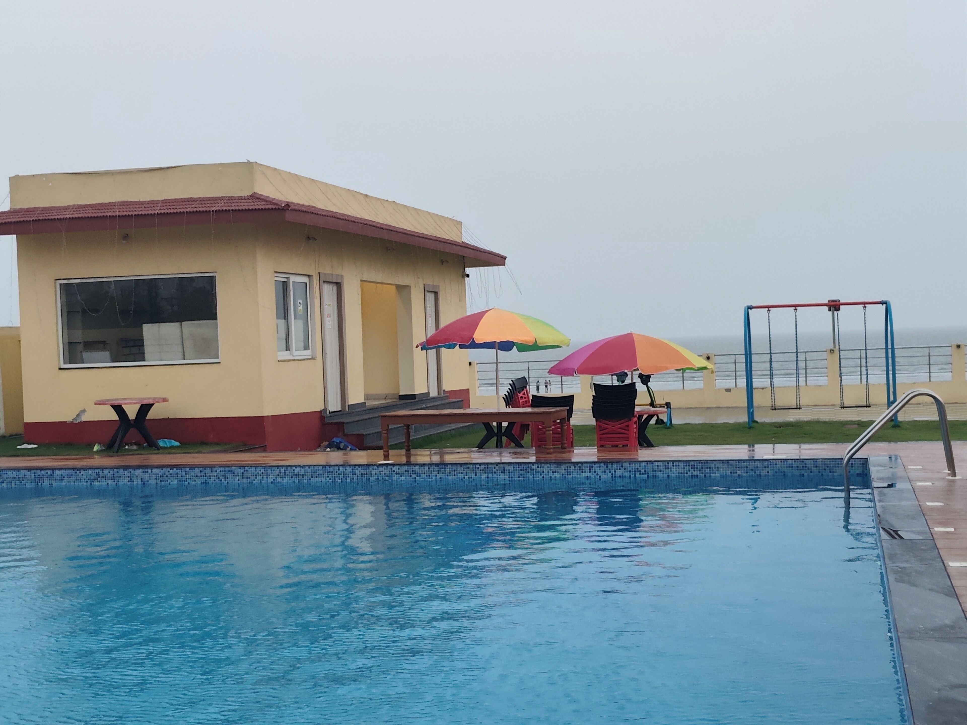 A swimming pool with a small building, outdoor seating, and a swing set.