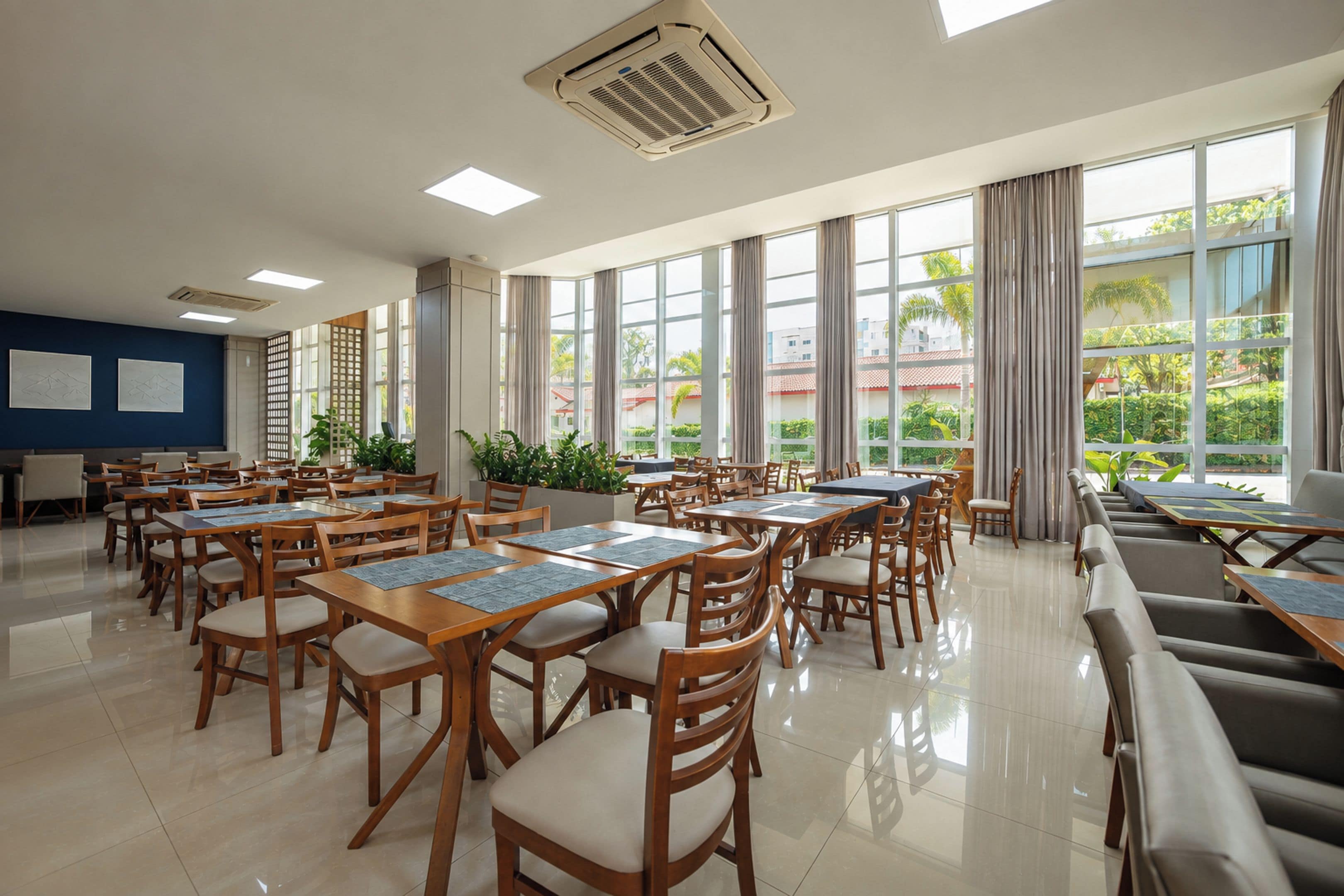 Una amplia sala de conferencias con múltiples mesas y sillas, ventanas grandes con cortinas y vistas al exterior.