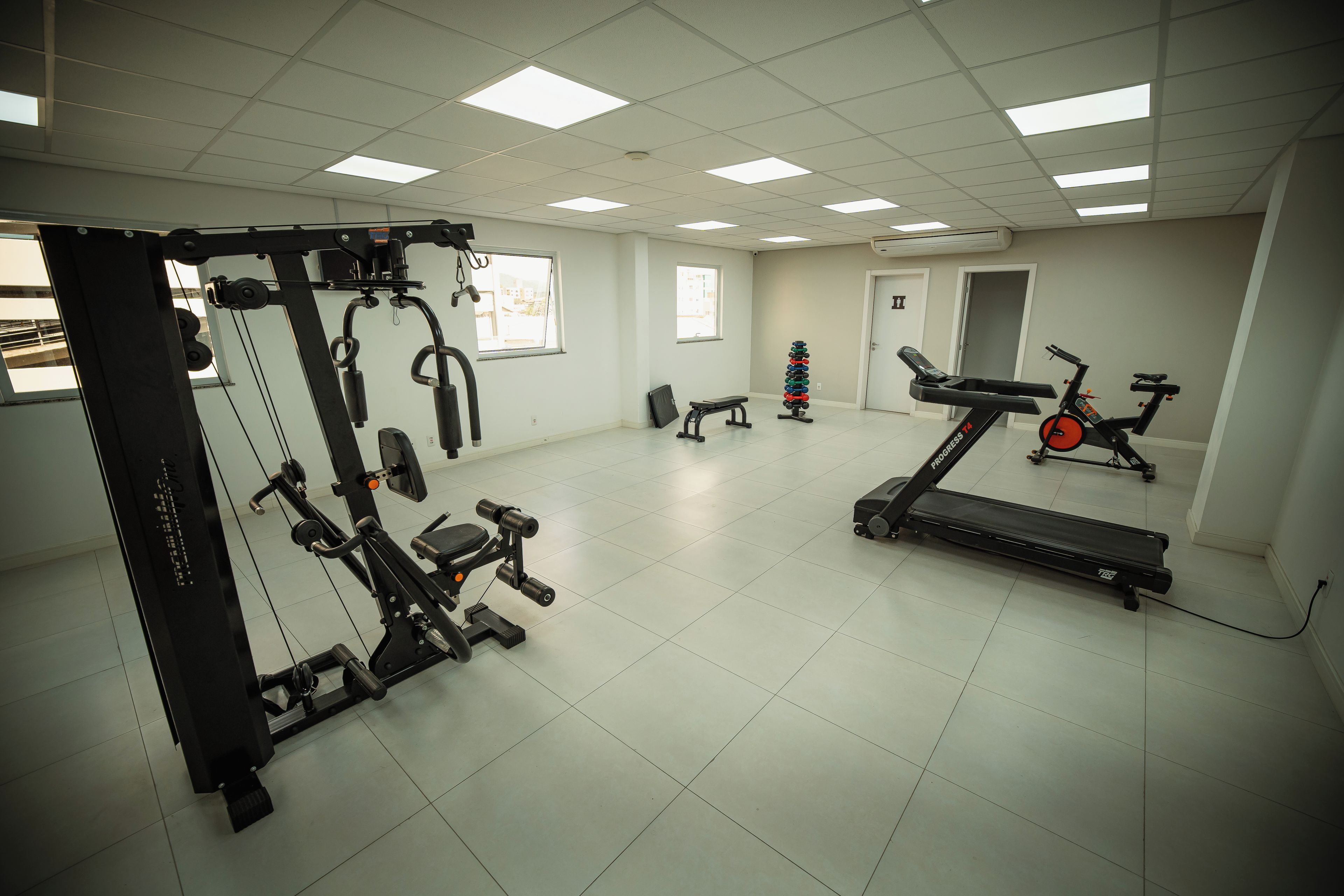 Un gimnasio con diversos equipos de ejercicio, incluyendo una cinta de correr, máquinas de pesas y un banco.
