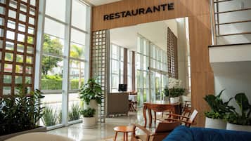 Un interno moderno con un cartello di legno che riporta la scritta 'RESTAURANTE' sopra una porta, che dà accesso a una sala da pranzo con tavoli e sedie.