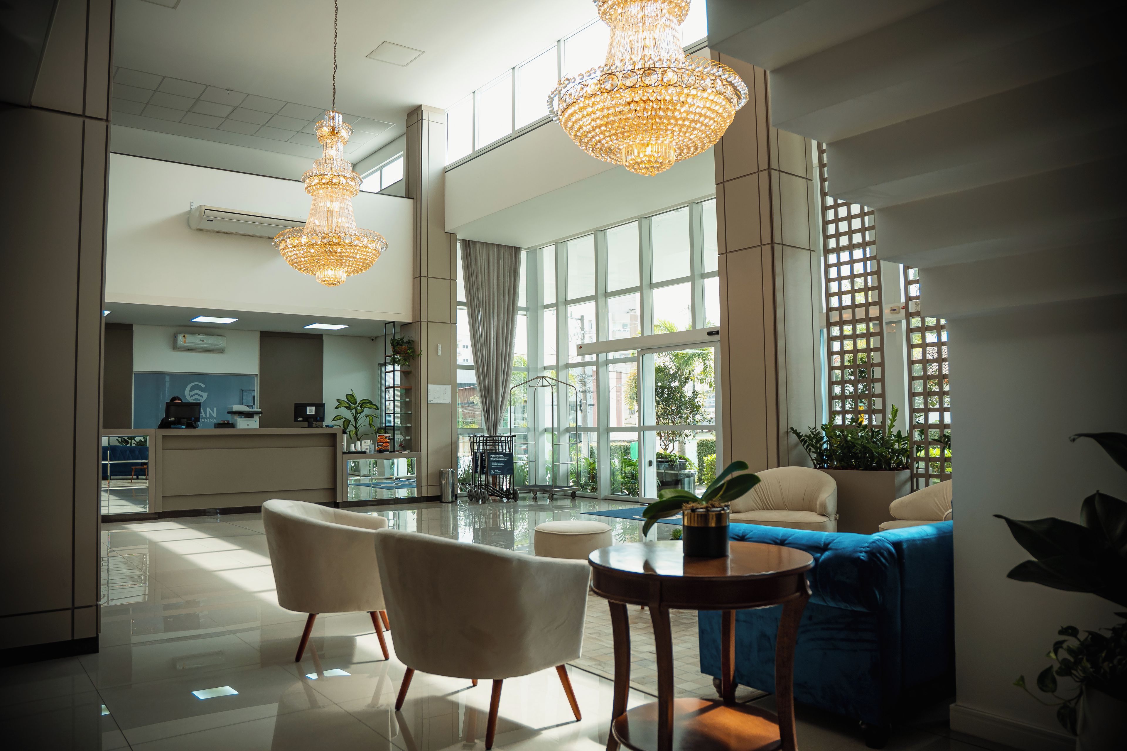 Um hall amplo com balcão de recepção, área de estar e grandes janelas que permitem a entrada de luz natural.