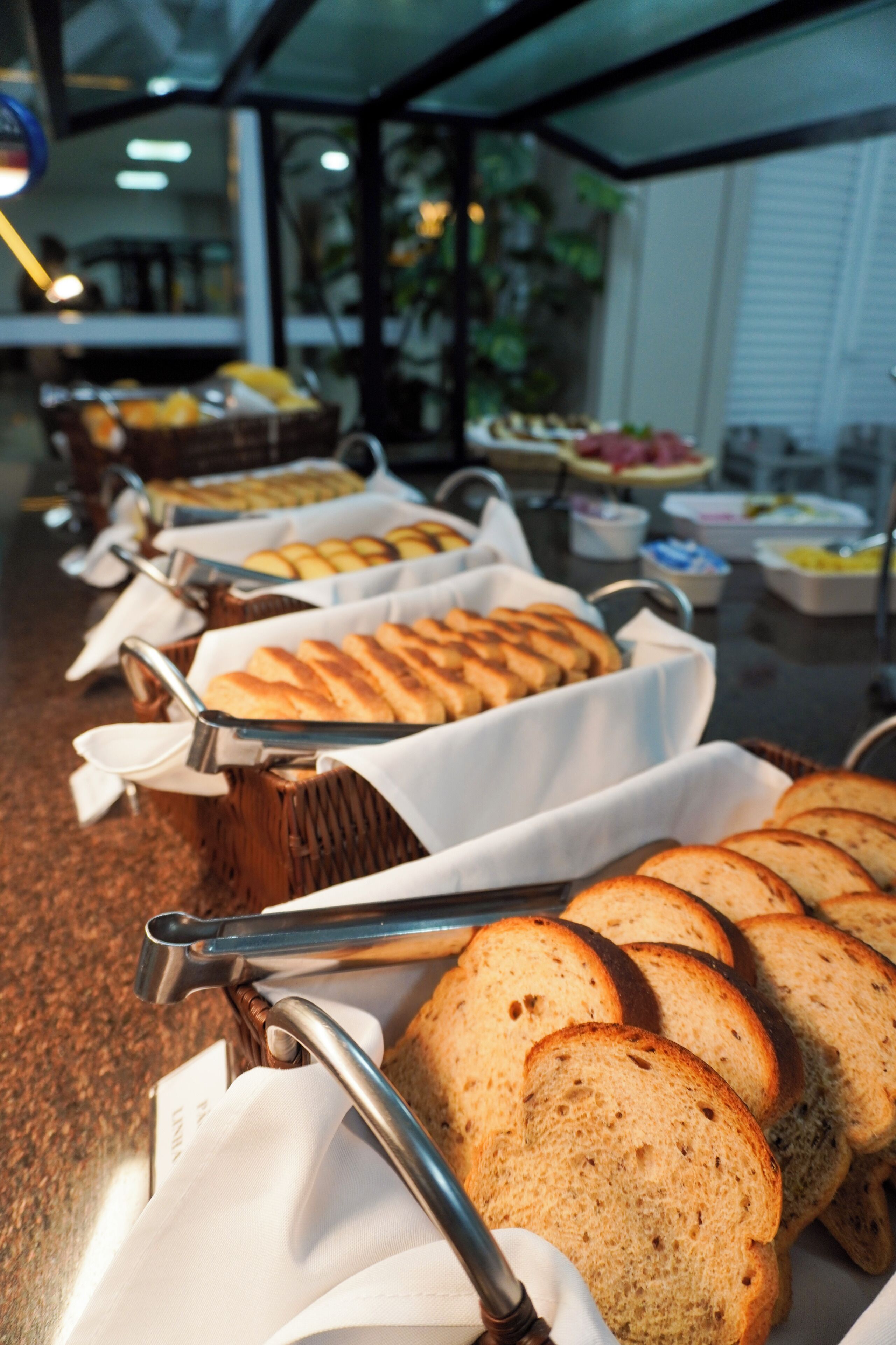 A buffet with various food items, including bread and pastries, arranged on tables with serving utensils.