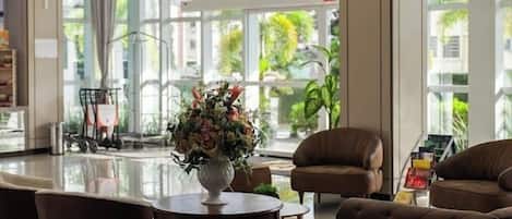 A spacious lobby with a large chandelier, a round table with chairs, and a view of the outdoors through large windows.