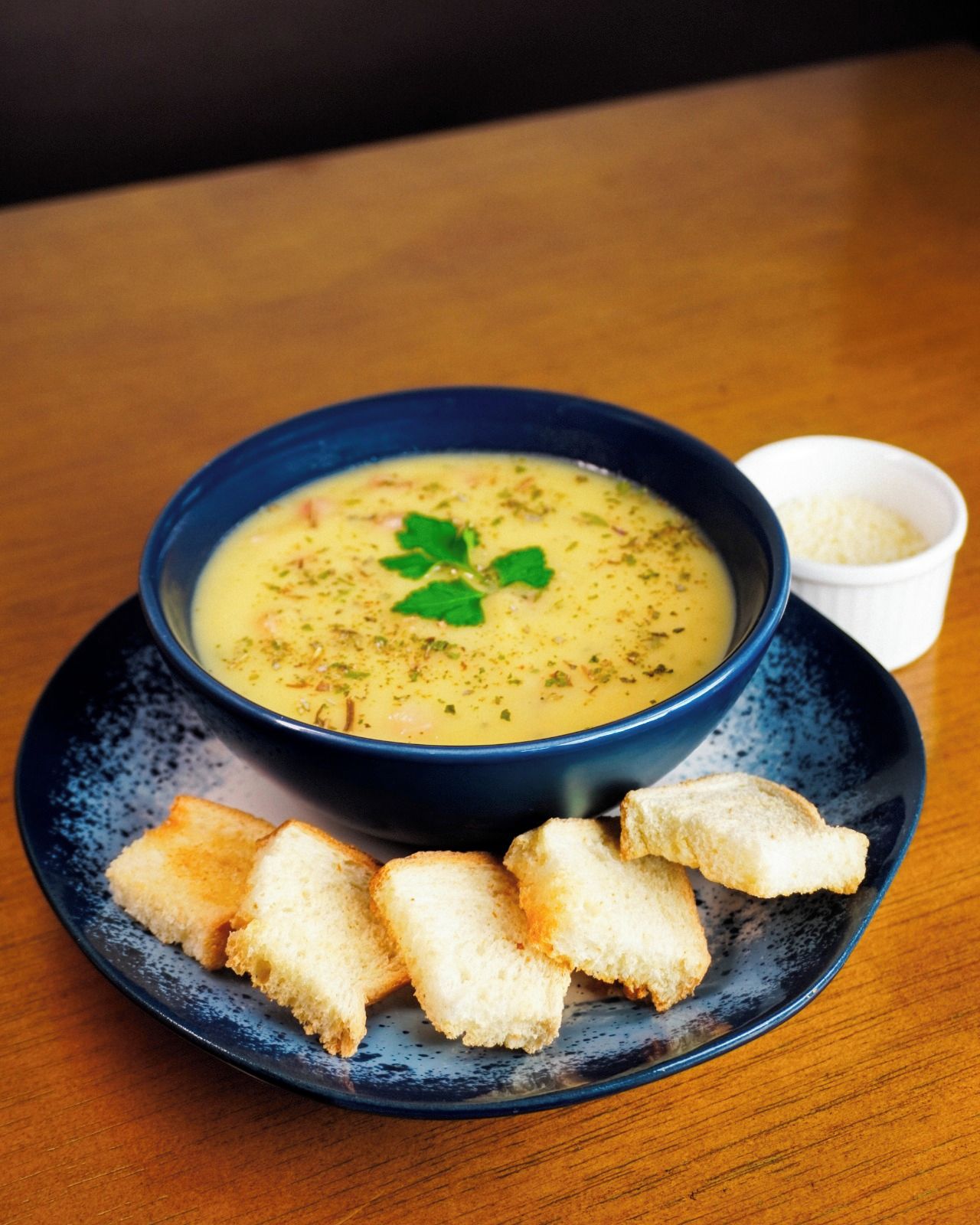 A bowl of soup on a plate with a small bowl of rice and some breadsticks.