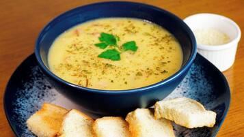 A bowl of soup on a plate with a small bowl of rice and some breadsticks.