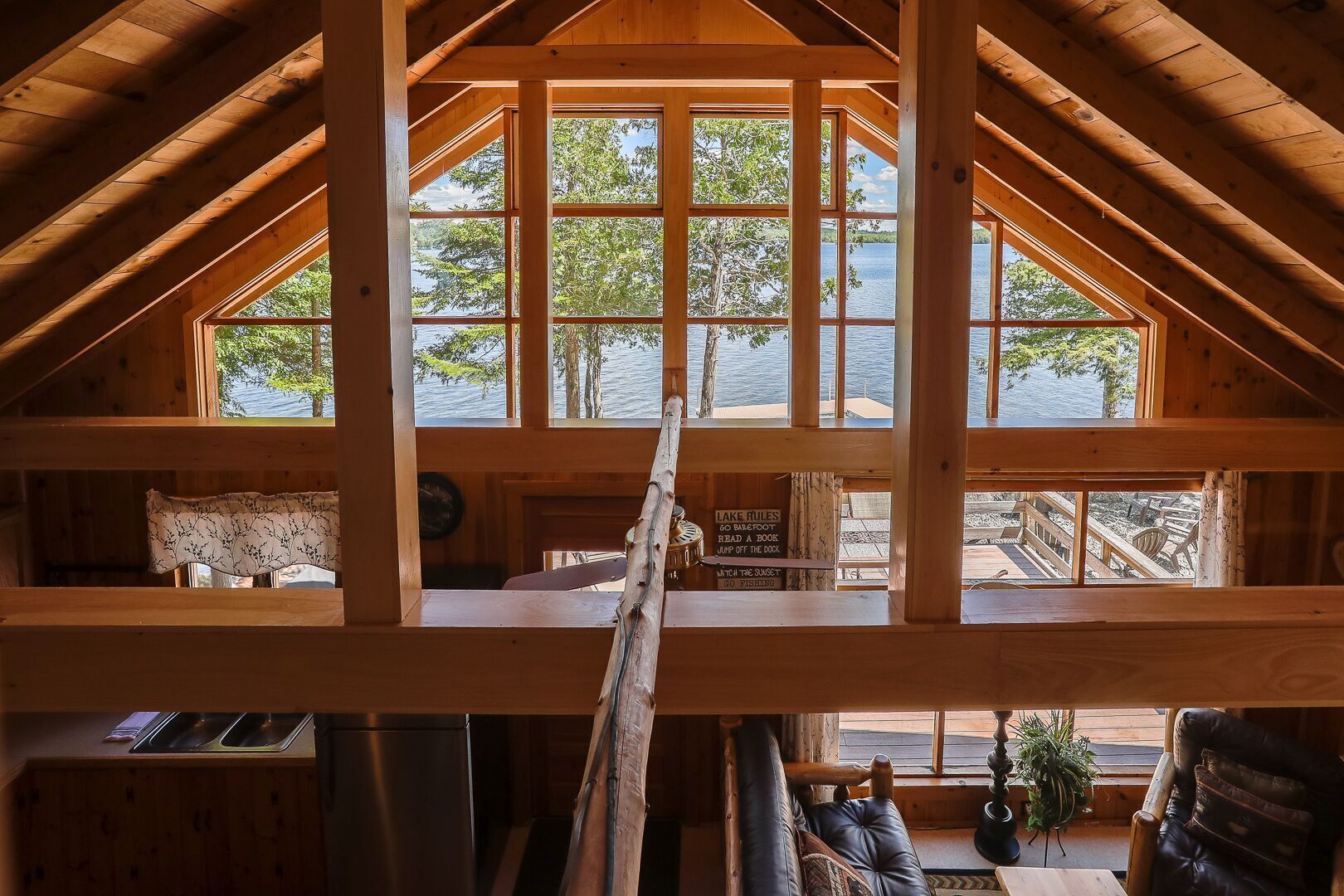 Une cabane avec une chambre à coucher située en mezzanine, de grandes fenêtres, une échelle en bois et une vue sur un quai et un lac.