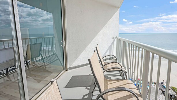 A balcony with a glass door, a metal railing, and a view of the beach. - Renovated Oceanview Studio Steps from Ocean Annies (Myrtle Beach)