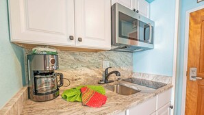 A kitchen with white cabinets, a stainless steel coffee maker, a microwave, and a sink. - Renovated Oceanview Studio Steps from Ocean Annies (Myrtle Beach)