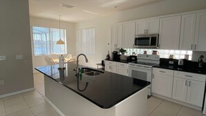 Uma cozinha moderna com armários brancos, bancada preta, pia de aço inoxidável e micro-ondas embutido.
