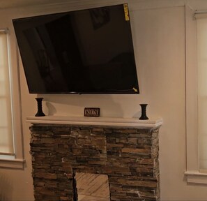 A living room with a stone fireplace, a flat-screen TV mounted above it, and a sign on the mantel that reads "ENERGY". - Master's Ready Phenomenal 3-bedroom 2 bath house in charming Augusta (Augusta)