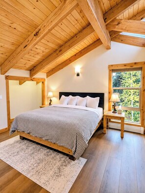 A bedroom with a wooden ceiling, a bed with a checkered bedspread, bedside lamps, and a window with a view of greenery. - 5BR Lodge, 1mi to Ski, HotTub, PoolTable, Firepit, Sleeps 12, Easy Access (Durango)
