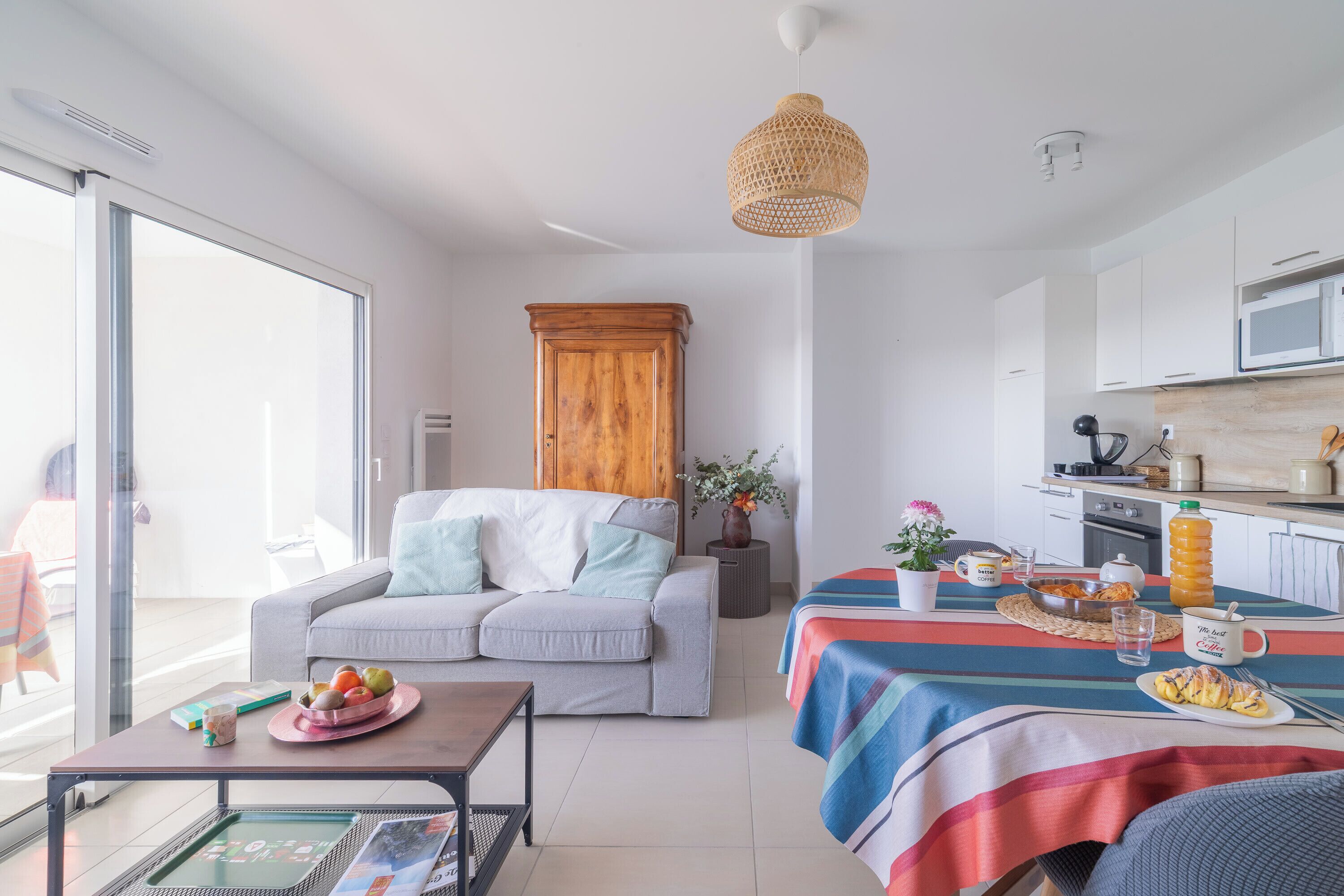 Un salon moderne avec un canapé, une table basse et un coin repas où la table est mise pour le petit-déjeuner.