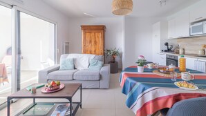 A modern living room with a sofa, coffee table, and a dining area with a table set for breakfast. - L’Hortus – Vue montagnes - Balcon (Saint-Mathieu-de-Tréviers)